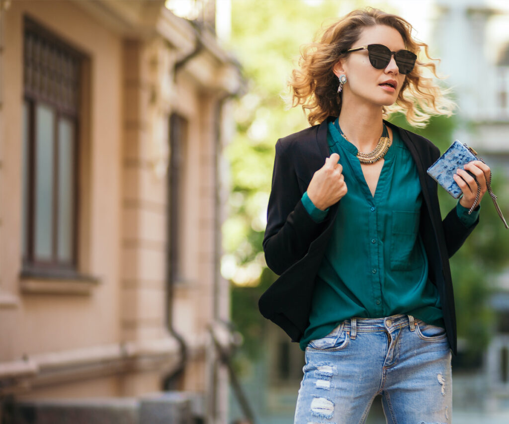 A woman in sunglasses and a jacket holding a cell phone.
