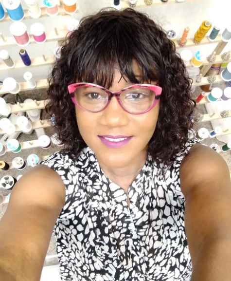 A woman with glasses and curly hair in front of many bottles.