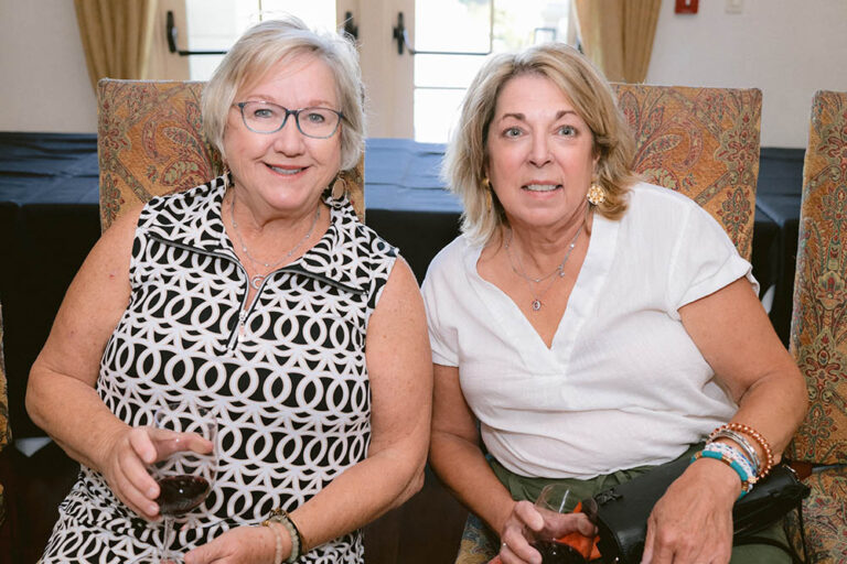 Two women sitting next to each other holding drinks.