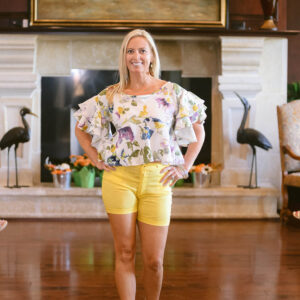 A woman standing in front of a fireplace wearing yellow shorts.