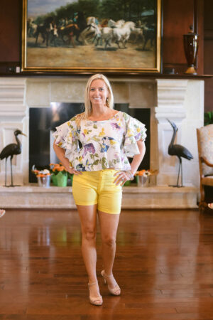 A woman standing in front of a fireplace wearing yellow shorts.