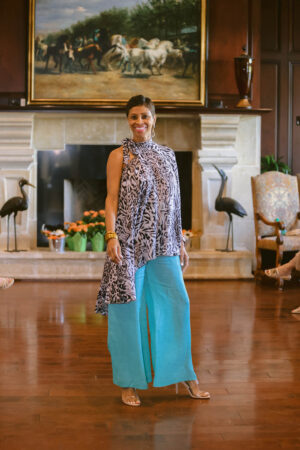 A woman standing in front of a fireplace wearing blue pants.