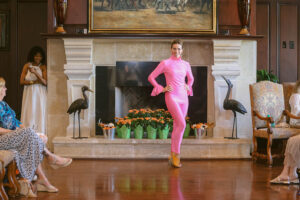 A woman in pink standing next to a fireplace.