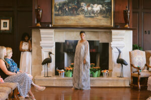 A woman in a long dress standing next to an open fireplace.