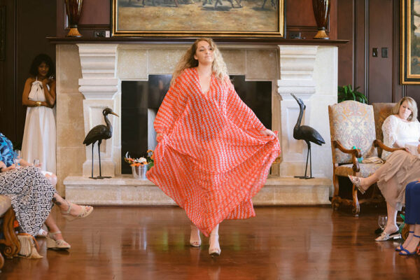 A woman in an orange and white dress standing on the floor.