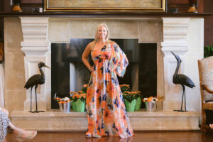 A woman in an orange and blue dress standing next to a fireplace.