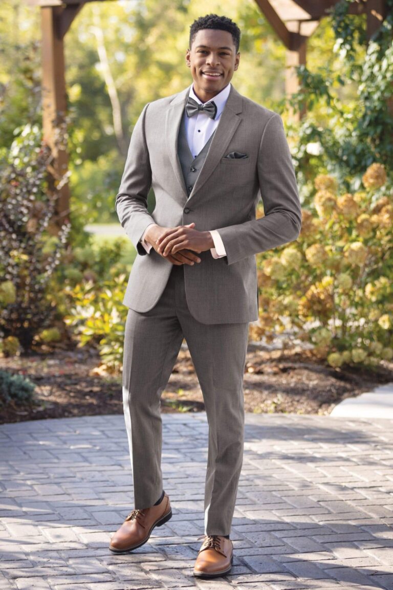 A man in a suit and bow tie standing on the sidewalk.