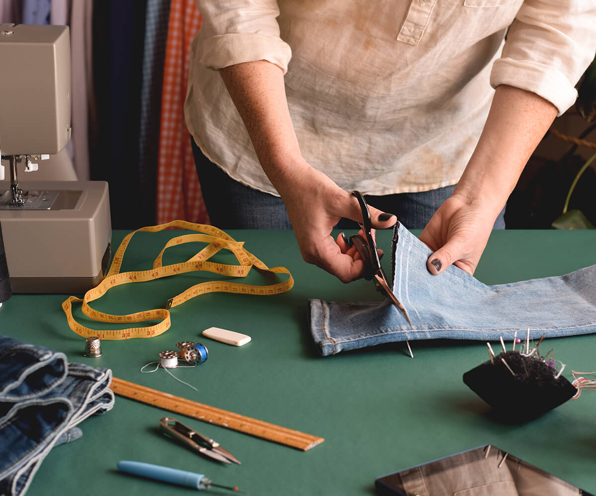 A person cutting fabric with scissors on top of table.